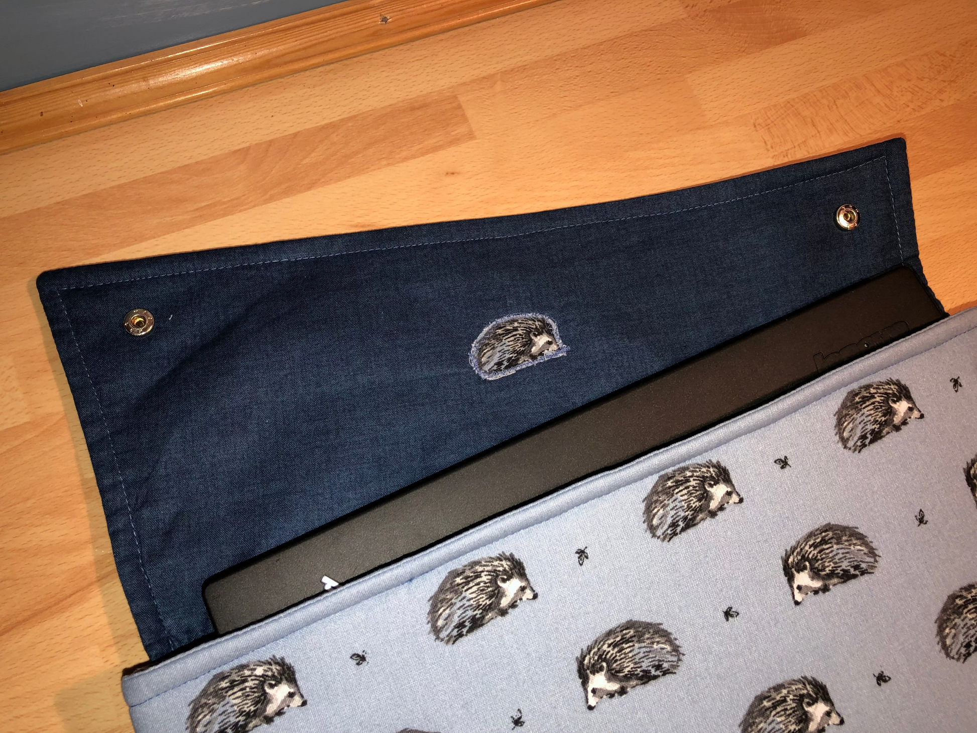 laptop sleeve with hedgehogs fabric and asymmetric darker blue flap fastened with studs.